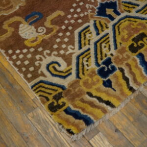 Brown rug with blue, yellow, and cream geometric and scroll patterns on worn wood floorboards.
