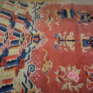 A rose field rug with scattered blue and yellow motifs features a colorful, striped, curvilinear border on wood flooring.