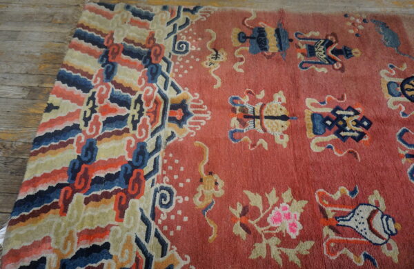 A rose field rug with scattered blue and yellow motifs features a colorful, striped, curvilinear border on wood flooring.