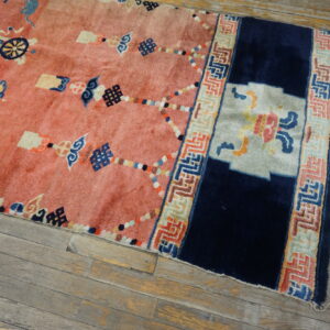 Plush pink rug with navy blue and multicolored Asian motifs and border on distressed wood plank flooring.