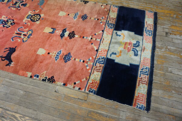 Plush pink rug with navy blue and multicolored asian motifs and border on distressed wood plank flooring.