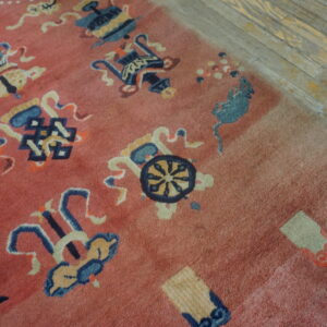 Detail of a faded pink rug with blue and cream stylized patterns resting on rustic wood planks.