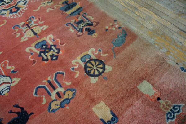 Detail of a faded pink rug with blue and cream stylized patterns resting on rustic wood planks.