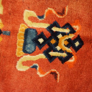 Thick, textured pile rug detail in red-orange featuring stylized designs in dark blue, cream, and yellow.