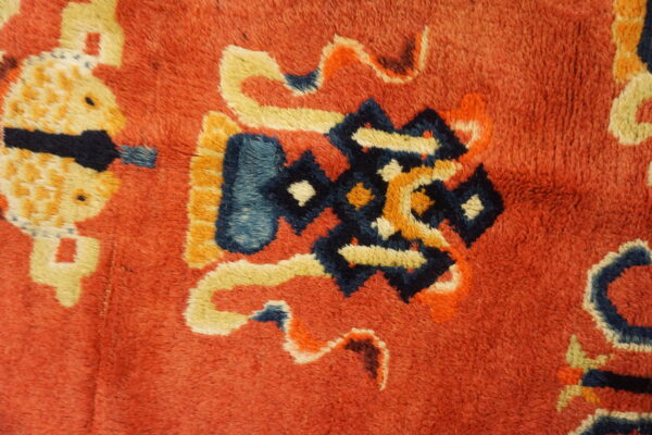 Thick, textured pile rug detail in red-orange featuring stylized designs in dark blue, cream, and yellow.