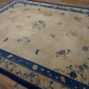 Beige area rug featuring blue floral sprays, wide blue borders, and set on rustic wood planks.
