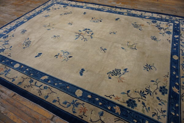 Beige area rug featuring blue floral sprays, wide blue borders, and set on rustic wood planks.