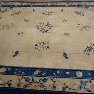 Pale gold area rug with scattered blue floral sprays and an extensive dark blue border on hardwood flooring.