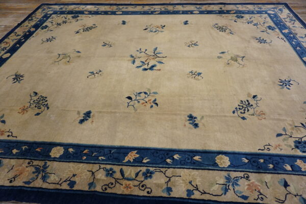 Pale gold area rug with scattered blue floral sprays and an extensive dark blue border on hardwood flooring.