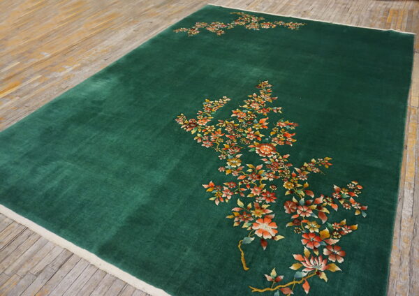 Green rug with plush pile displaying sweeping orange and yellow floral designs on worn hardwood.