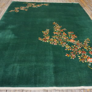 Deep green rug with high pile and light edges, displaying detailed orange and yellow florals on wood floor.