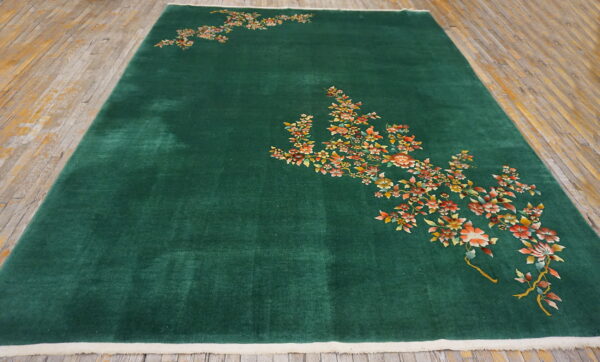Deep green rug with high pile and light edges, displaying detailed orange and yellow florals on wood floor.