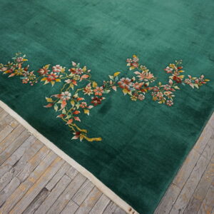 Emerald green rug with a blush and rust floral design lies on weathered wood planks.