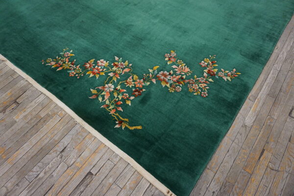 Emerald green rug with a blush and rust floral design lies on weathered wood planks.