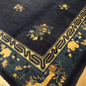 Navy blue rug with a yellow geometric and floral border, showing fringe on light wood floors.