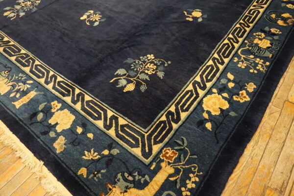 Navy blue rug with a yellow geometric and floral border, showing fringe on light wood floors.