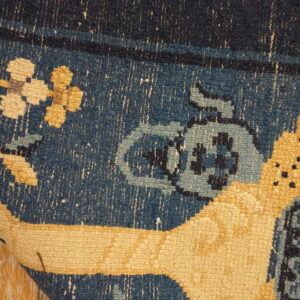 Detail of a blue and yellow patterned rug curled on peeling light wood planks.