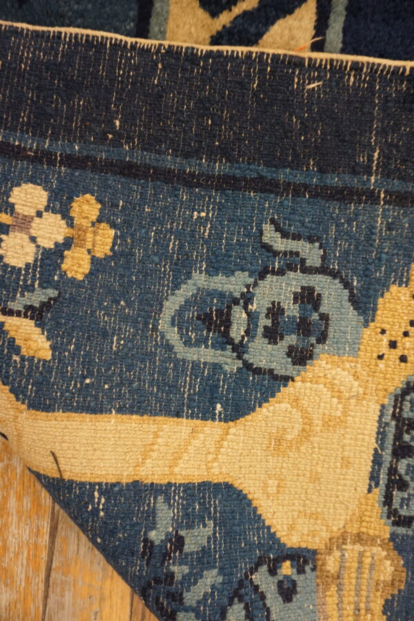 Detail of a blue and yellow patterned rug curled on peeling light wood planks.