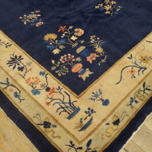 Navy blue rug corner showing colorful floral motifs and a wide tan border on distressed wood flooring.
