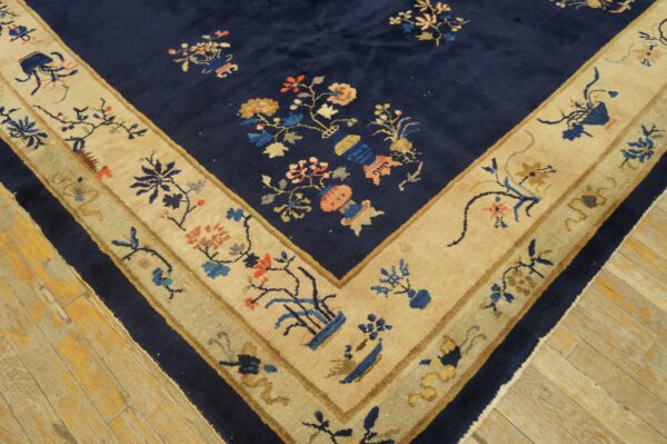 Navy blue rug corner showing colorful floral motifs and a wide tan border on distressed wood flooring.