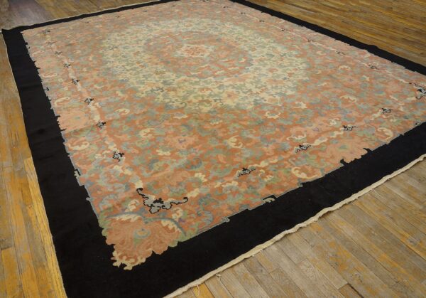 Oversized peach and sage floral rug with a wide black border, displayed on wide, distressed wooden planks.