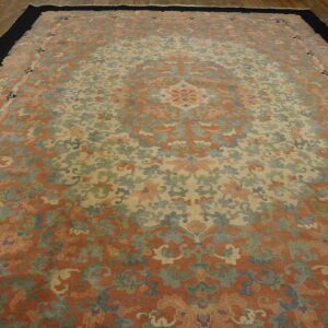 Low-pile rug with muted coral, cream, and sage floral motifs bordered in solid black on wood floors.