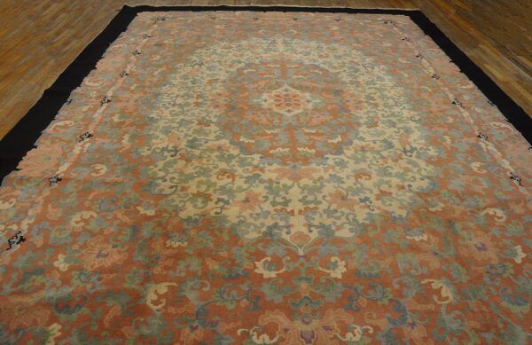 Low-pile rug with muted coral, cream, and sage floral motifs bordered in solid black on wood floors.