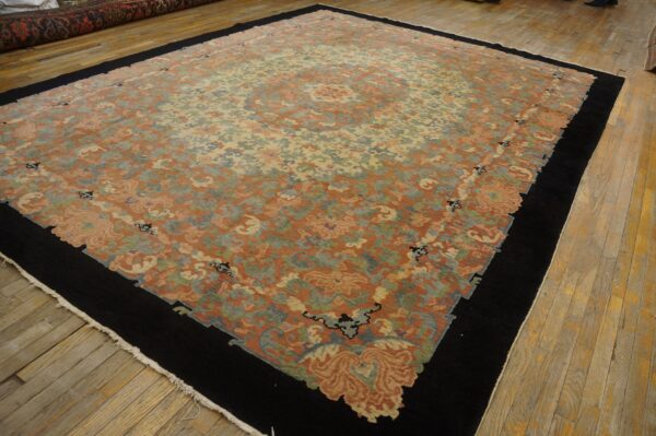Rust and cream floral rug featuring a black border and central medallion, displayed on worn wooden plank flooring.