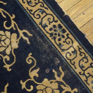 Navy blue rug with tan and light blue border designs lies on distressed light wood floors.