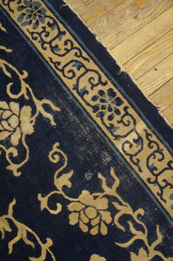 Navy blue rug with tan and light blue border designs lies on distressed light wood floors.