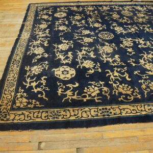 A large navy rug with gold floral and vine motifs lies on light-colored plank wood flooring.