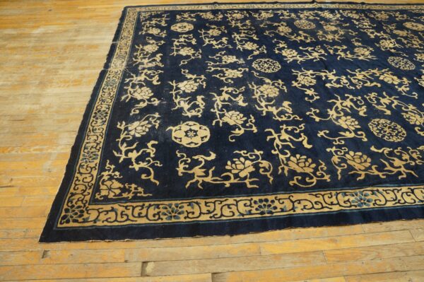 A large navy rug with gold floral and vine motifs lies on light-colored plank wood flooring.