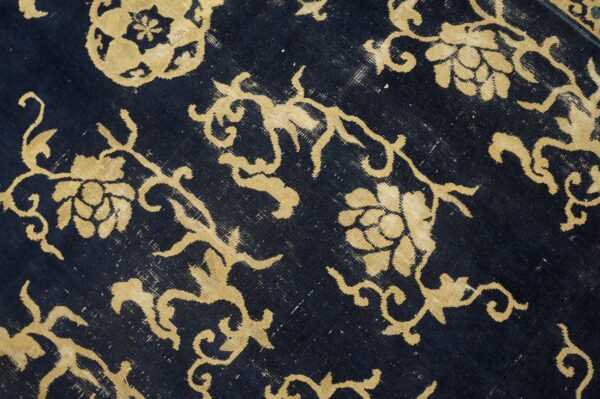 Distressed rug with golden floral and vine motifs against a faded dark blue, low-pile background.