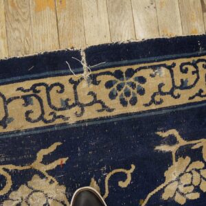 Detail of a dark blue and tan floral rug on light wood flooring, with a visible shoe toe.
