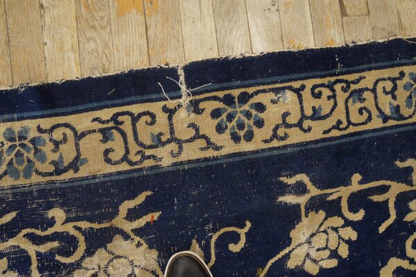 Detail of a dark blue and tan floral rug on light wood flooring, with a visible shoe toe.