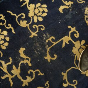 Distressed navy rug with yellow floral designs and a partial black shoe visible on the edge.