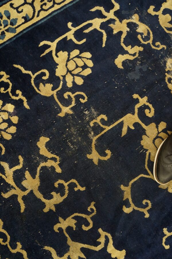 Distressed navy rug with yellow floral designs and a partial black shoe visible on the edge.
