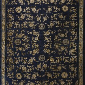 Ornate dark blue rug with a gold scrolling vine motif covering the low-pile field and border.