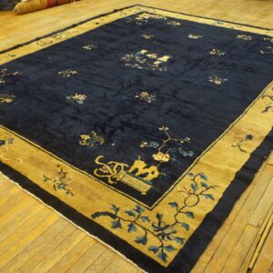 Navy blue rug with a gold border and intricate floral and vase patterns lies on light hardwood floor.