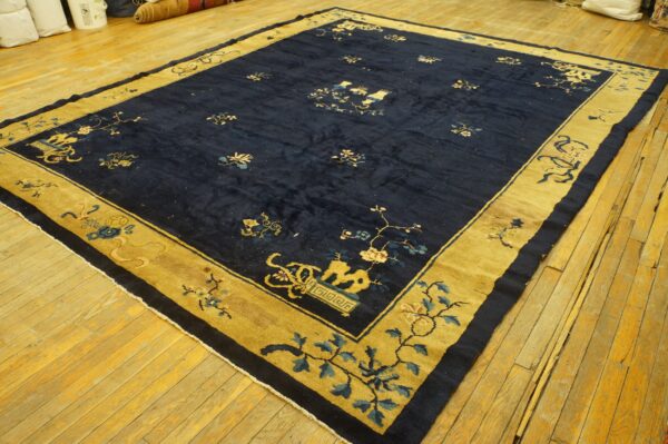 Navy blue rug with a gold border and intricate floral and vase patterns lies on light hardwood floor.