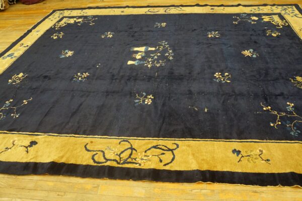 Large navy blue rug with stylized floral motifs and a broad mustard yellow pictorial border on a wood floor.
