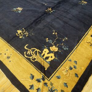A deep navy rug with scattered yellow and blue flowers and a wide gold floral border on wood floors.