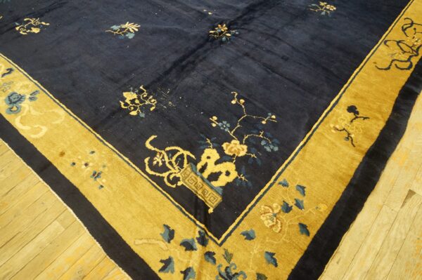 A deep navy rug with scattered yellow and blue flowers and a wide gold floral border on wood floors.