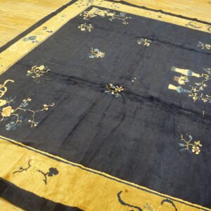 Dark blue low-pile rug with scattered floral designs and a wide mustard-gold patterned border on wood floors.