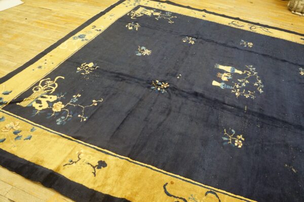 Dark blue low-pile rug with scattered floral designs and a wide mustard-gold patterned border on wood floors.