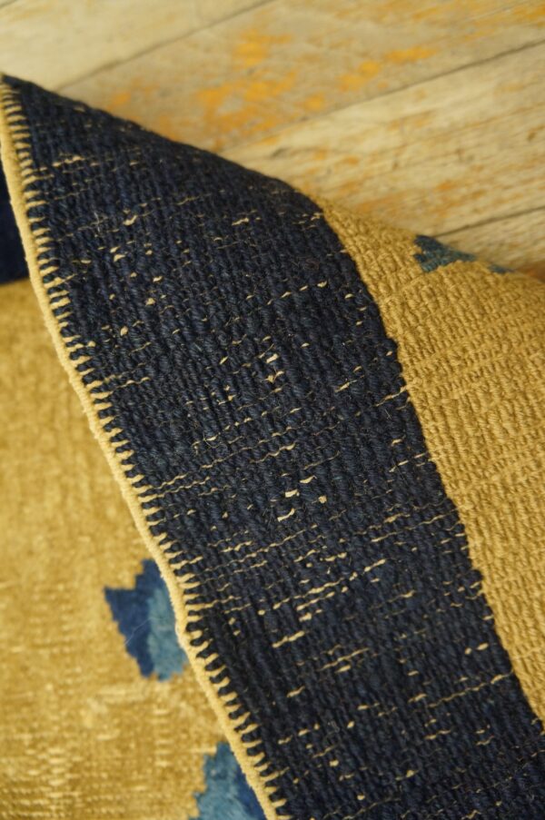 Coarse flatweave rug corner, featuring navy blue and mustard tones, resting on distressed painted wood.