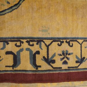 Golden yellow rug detail showing dark blue stylized border motifs and a reddish-brown outer band on wood planks.