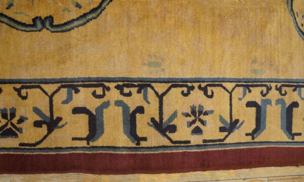 Golden yellow rug detail showing dark blue stylized border motifs and a reddish-brown outer band on wood planks.