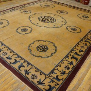 Square mustard rug with navy floral medallions and a burgundy border resting on light wood flooring.