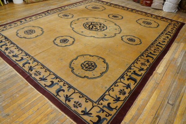 Square mustard rug with navy floral medallions and a burgundy border resting on light wood flooring.